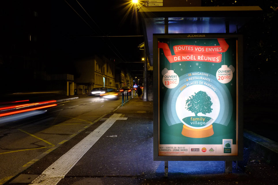 Photographie de nuit d'une affiche abribus  illuminée pour les fêtes de Noël. L'affiche représente une boule à neige avec un arbre à l'intérieur
